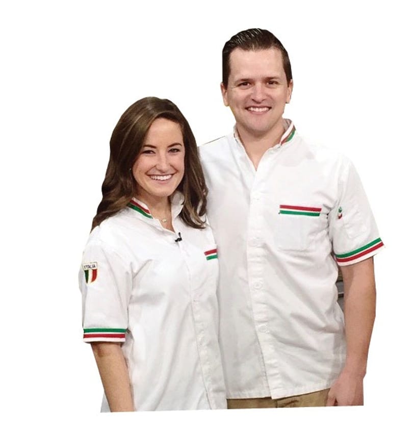 Two smiling chefs, a woman and a man, wearing white uniforms with Italian flag accents.