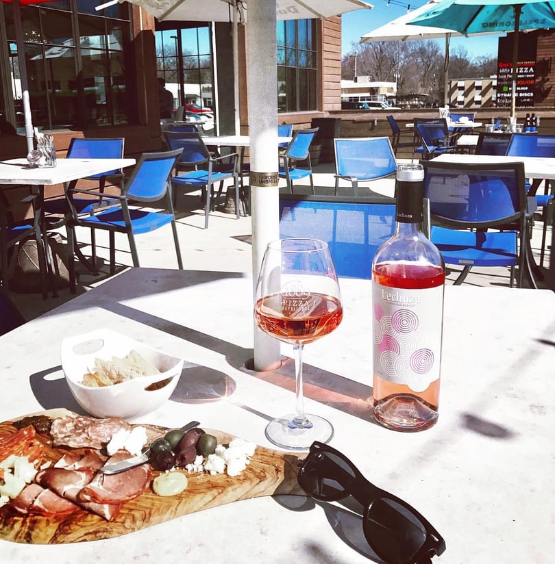 Charcuterie board with meats, cheeses, and olives, a glass of rosé, and a bottle of Lechuza wine on an outdoor patio table.